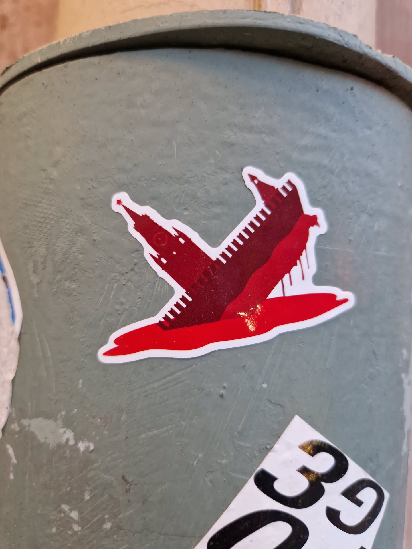 A sticker depicting a minimalist illustration of the Kremlin towers submerged or bleeding in a pool of red, possibly symbolizing conflict or political turmoil.  The style is simple and graphic.