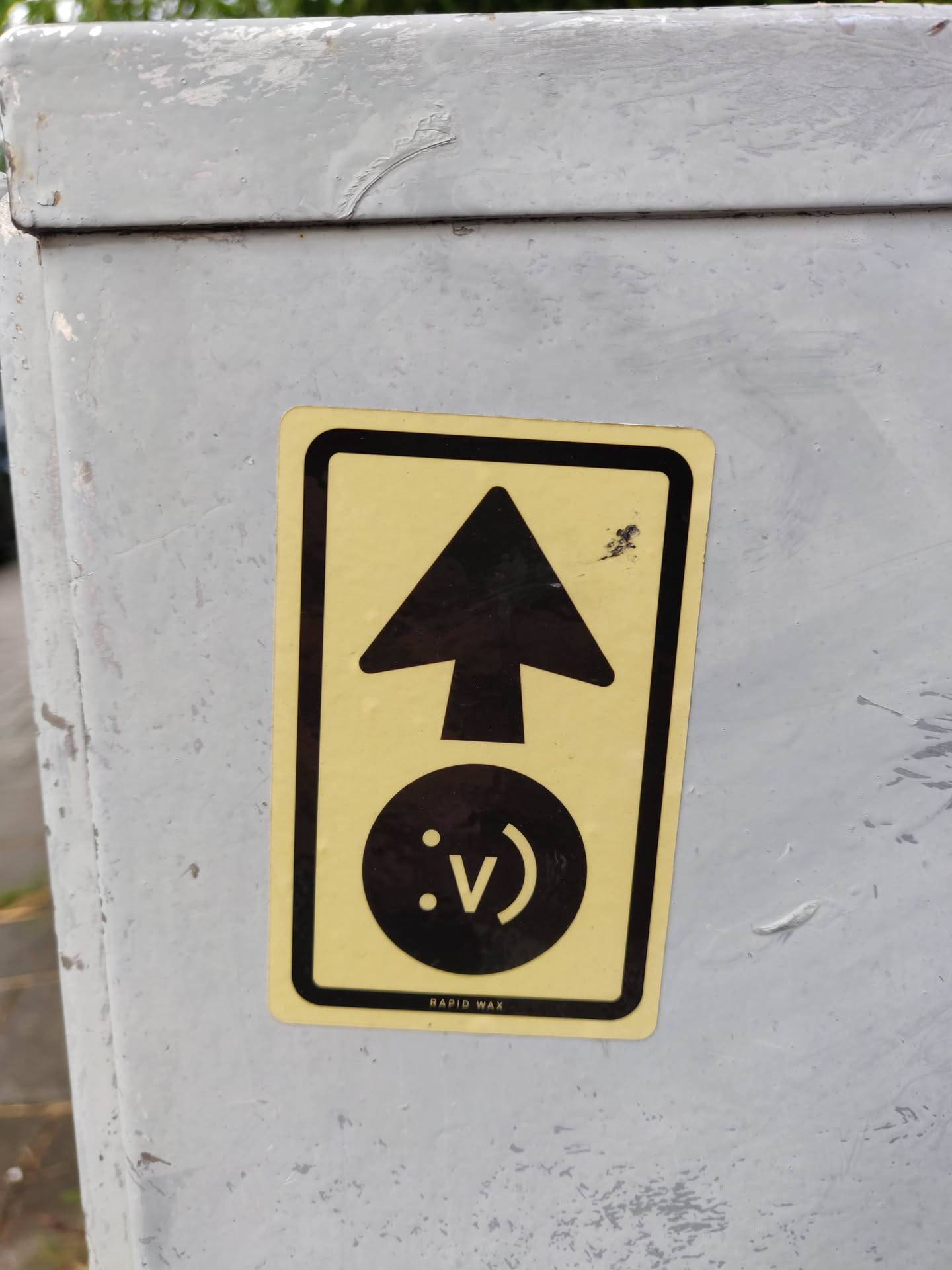 A yellow sticker with a black upward arrow and a smiley face with a V-shaped mouth.  The text "RAPID WAX" is visible at the bottom.
