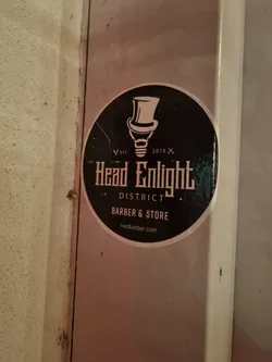 Street sticker Round sticker with a black background and white design.  It features an illustration of a lightbulb in a top hat, the text "Headlight District", "Barber & Store", and the website address. 