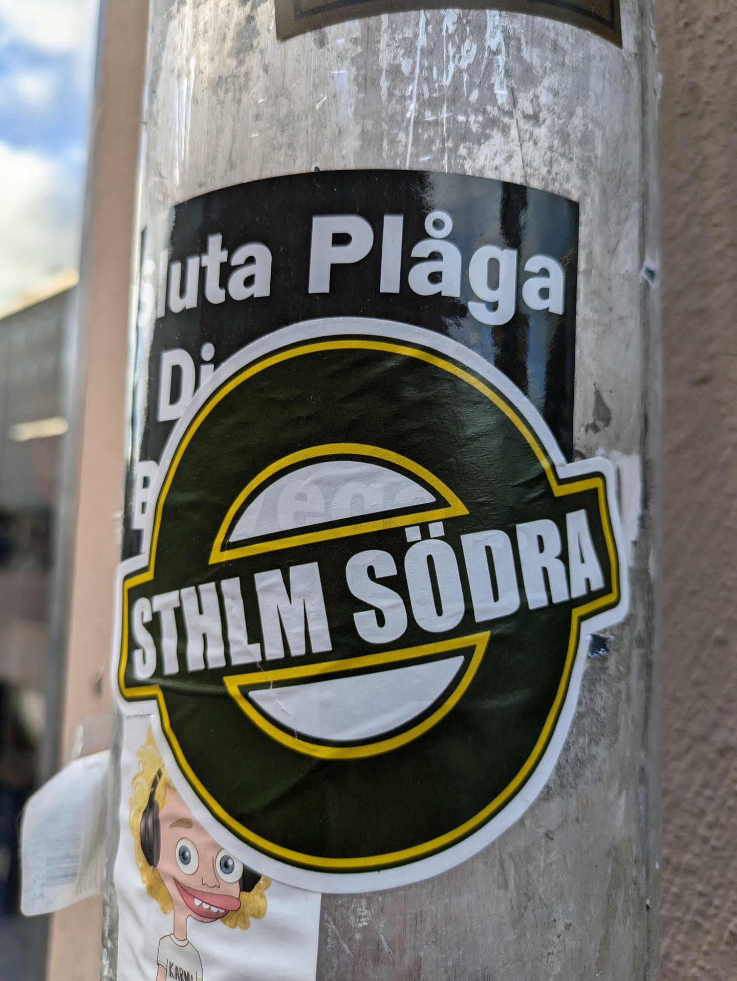 A dark green and yellow sticker with the text "STHLM SÖDRA" in white lettering.  Part of a larger sticker is visible above, showing the words "Sluta Plåga Djuren" (Stop Torturing Animals).