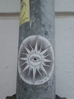 Oval sticker with a detailed illustration of an eye in the center of a sunburst design.  The style is reminiscent of vintage or occult imagery.  A small Instagram handle is visible at the bottom.