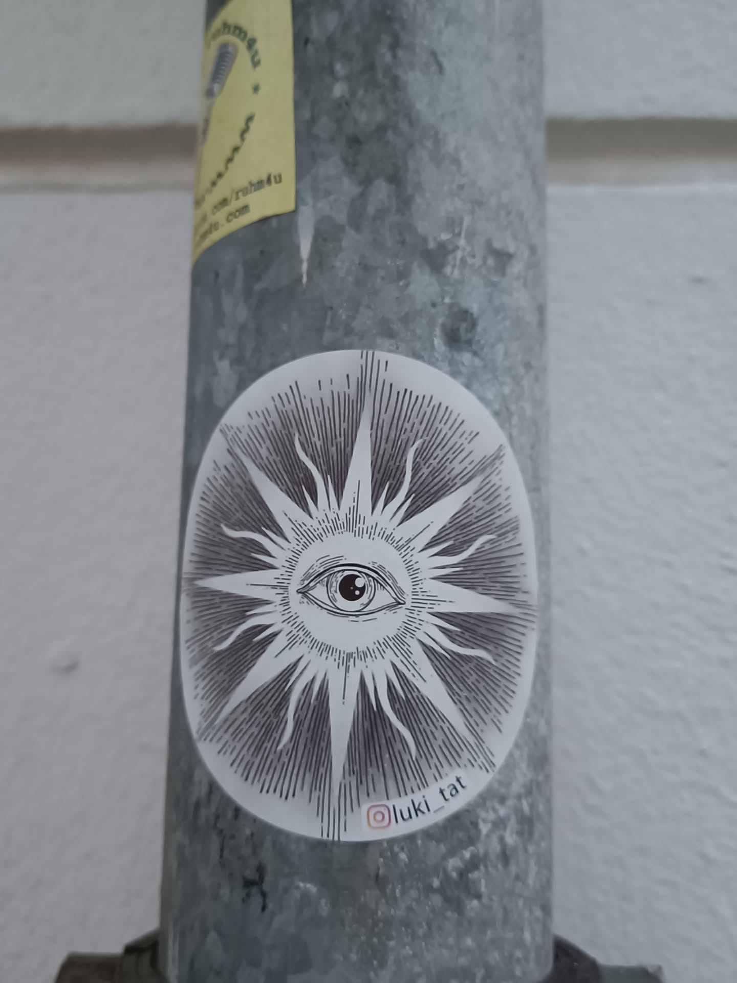 Oval sticker with a detailed illustration of an eye in the center of a sunburst design.  The style is reminiscent of vintage or occult imagery.  A small Instagram handle is visible at the bottom.