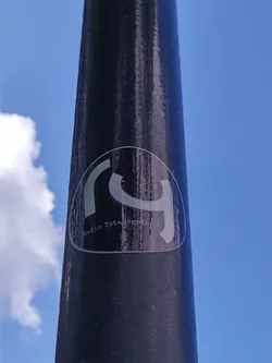 A black and white sticker with a logo and text on a dark pole. The sky is visible in the background.