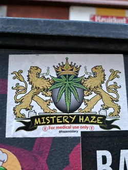 Sticker featuring a coat of arms design with two lions, a crown, and a cannabis leaf. The text 'Mystery Haze' is prominently displayed, along with the statement 'For medical use only'.  A social media handle is also included.