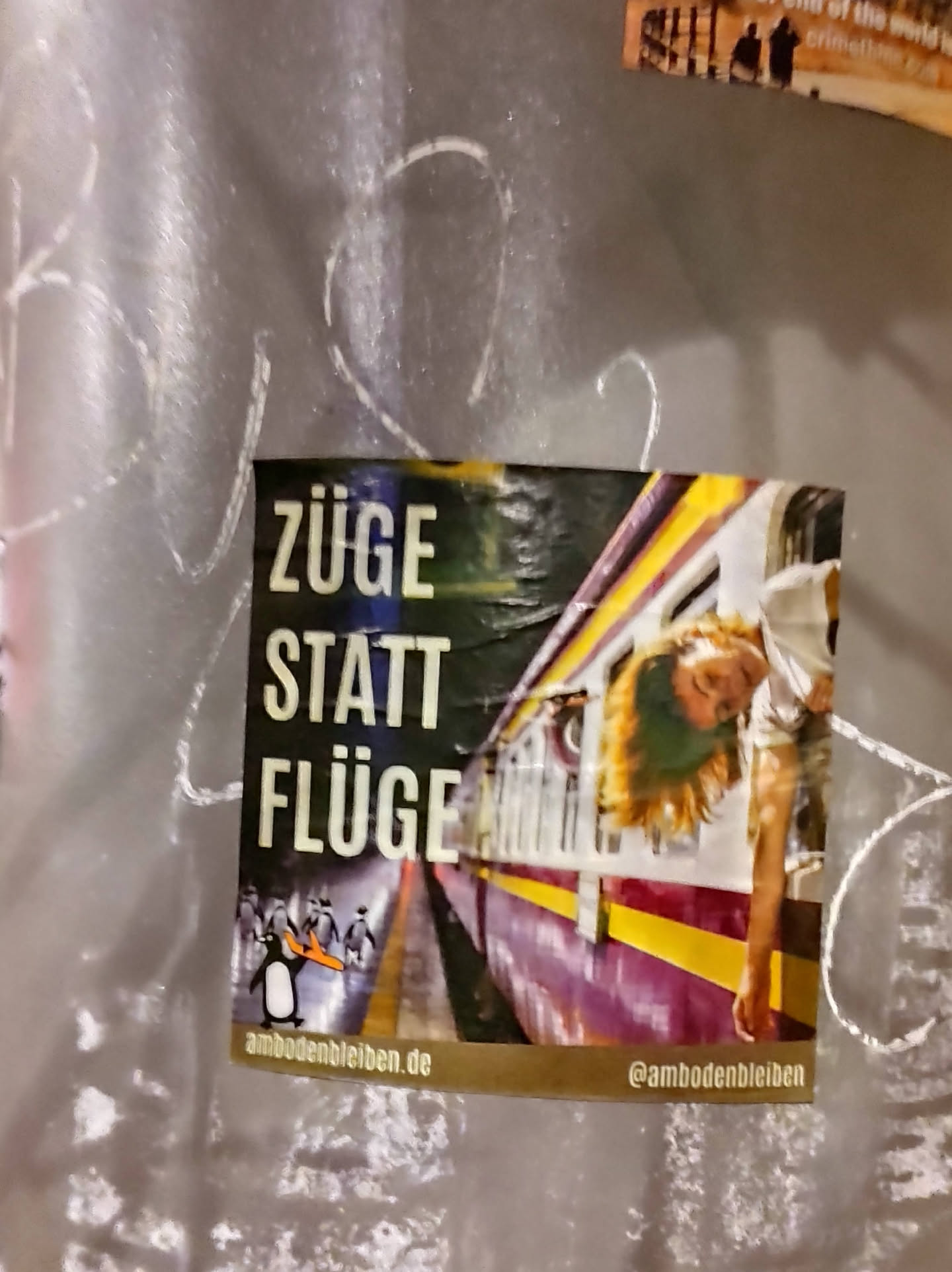 A square sticker featuring a photograph of a young woman leaning out of a train window. The main text on the sticker says "Züge statt Flüge" which translates from German to "Trains instead of planes".  A small penguin logo is visible at the bottom. A website and Instagram handle are also included. 