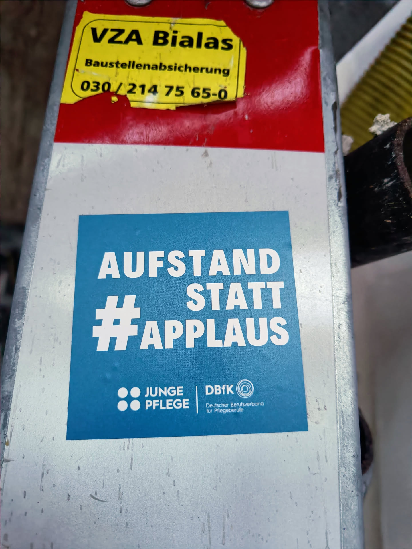 A blue sticker promoting a movement with the slogan "Aufstand statt Applaus" (Rebellion instead of applause). It features the logos of Junge Pflege (Young Care) and DBfK (German Federation of Professionals in the Health and Welfare Sector).
