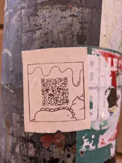 This sticker features a quirky design with a hand-drawn style. At the bottom is a simple illustration of a taco or burrito, topped with some sort of sauce. Above the taco is a QR code.
