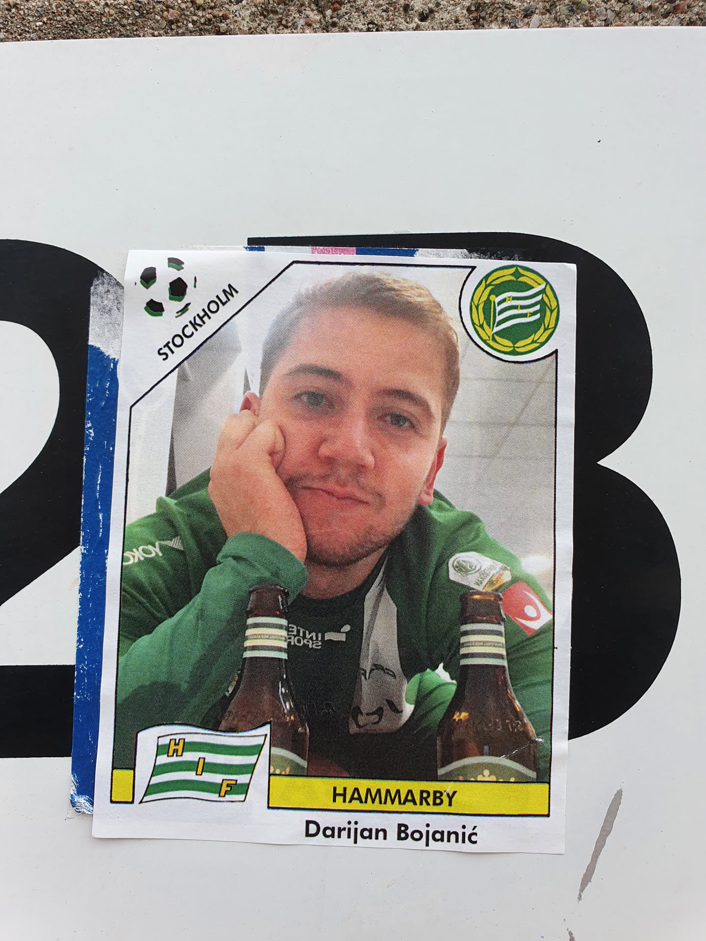 A sticker featuring a photo of Darijan Bojanić, seemingly a fan of the Hammarby football club. The sticker is designed to look like a trading card, with the Hammarby logo prominently displayed, along with a small flag depicting HIF.  The image shows Bojanić with two bottles of beer. The sticker was found in Stockholm, Sweden.