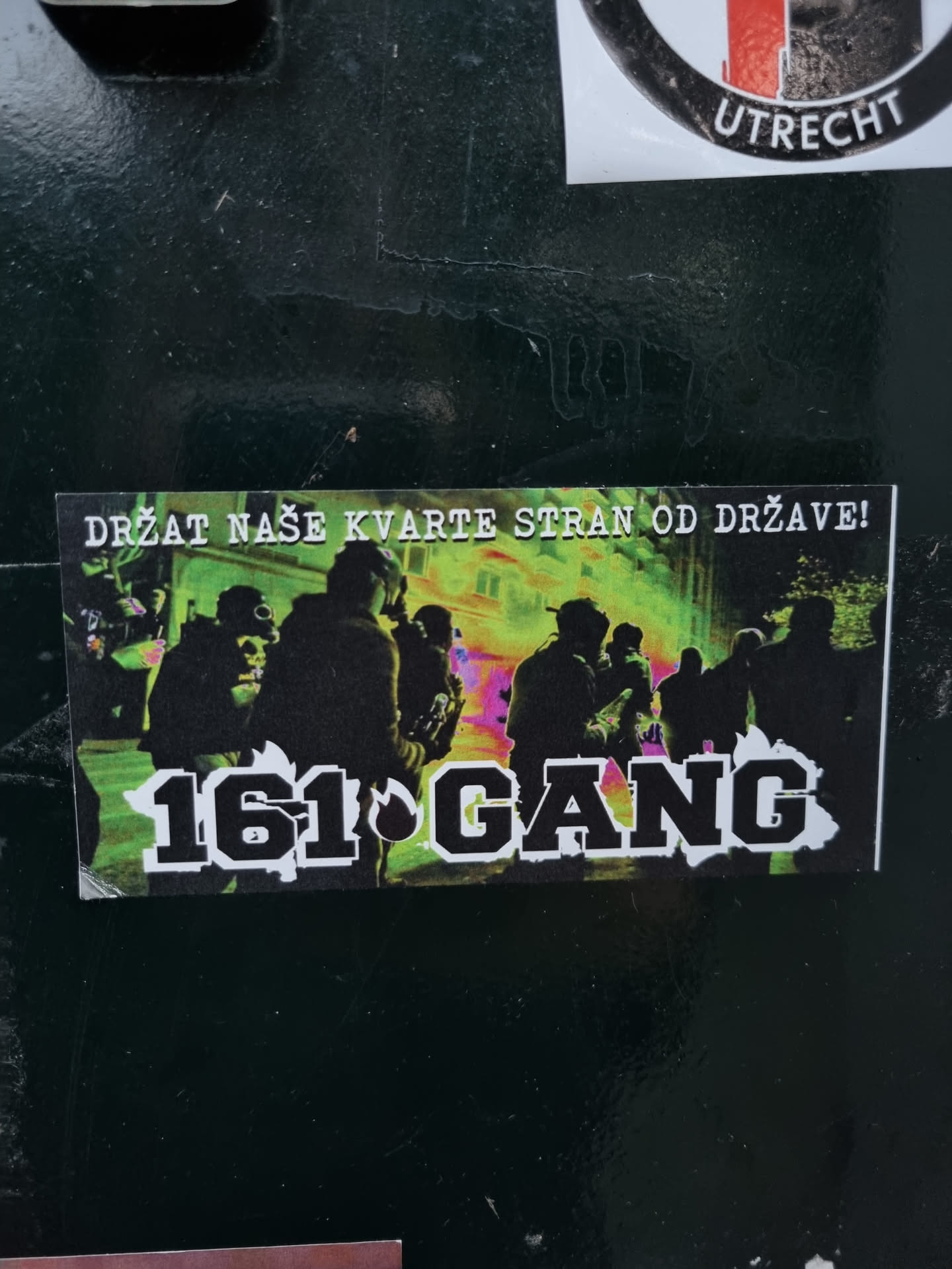 A sticker with a graphic design showing a group of people at night with a vibrant color scheme. The text '161 GANG' is prominently displayed in bold, uppercase letters.  The smaller text at the top says 'DRŽAT NAŠE KVARTE STRAN OD DRŽAVE!' which translates to 'Keep our neighborhoods away from the state!' in Croatian.