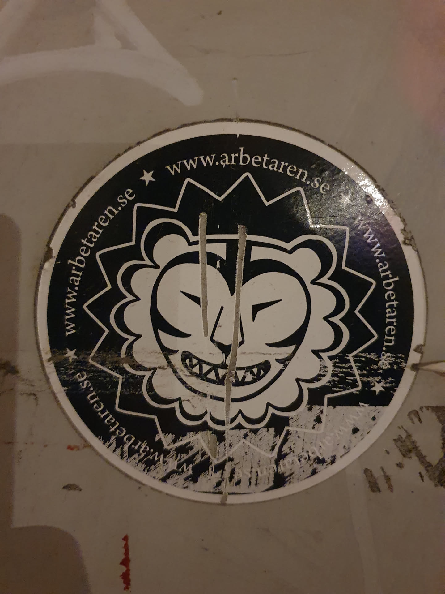 This is a circular sticker with a black and white illustration of a stylized lion's face. The lion has a fierce expression with sharp teeth. The background of the sticker is black, with white text circling the illustration that reads "www.arbetaren.se". The sticker shows signs of wear and tear.