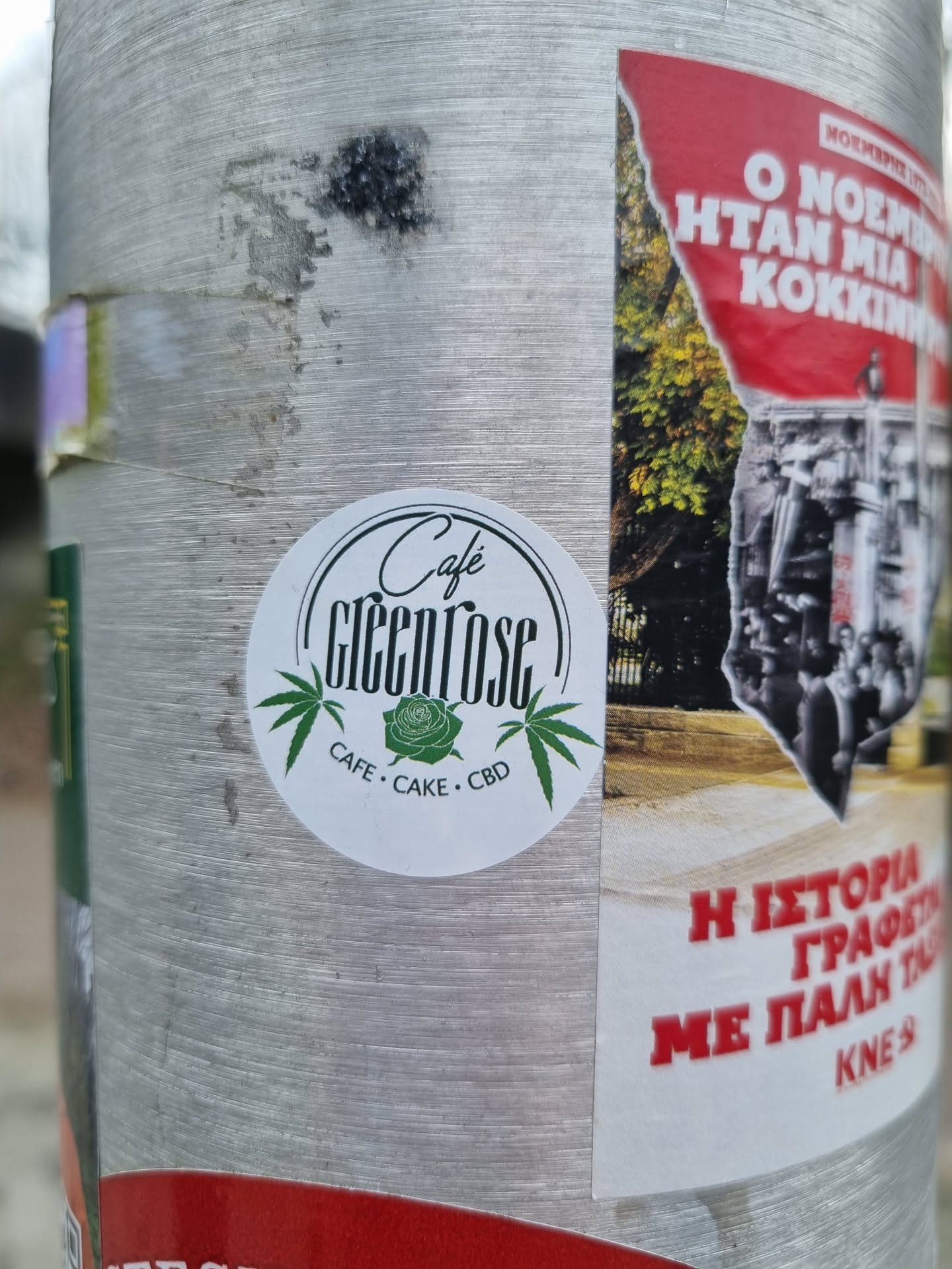 A round sticker advertising Cafe Greenrose, which offers cafe, cake, and CBD products. The sticker features a stylized rose and cannabis leaves.  The text 'Cafe Greenrose' is prominently displayed with 'CAFE · CAKE · CBD' underneath.