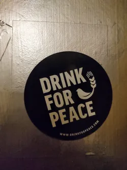 A round black sticker with the text "Drink for Peace" in white, accompanied by a small bird and wheat graphic.  The website www.drinkforpeace.com is printed at the bottom.