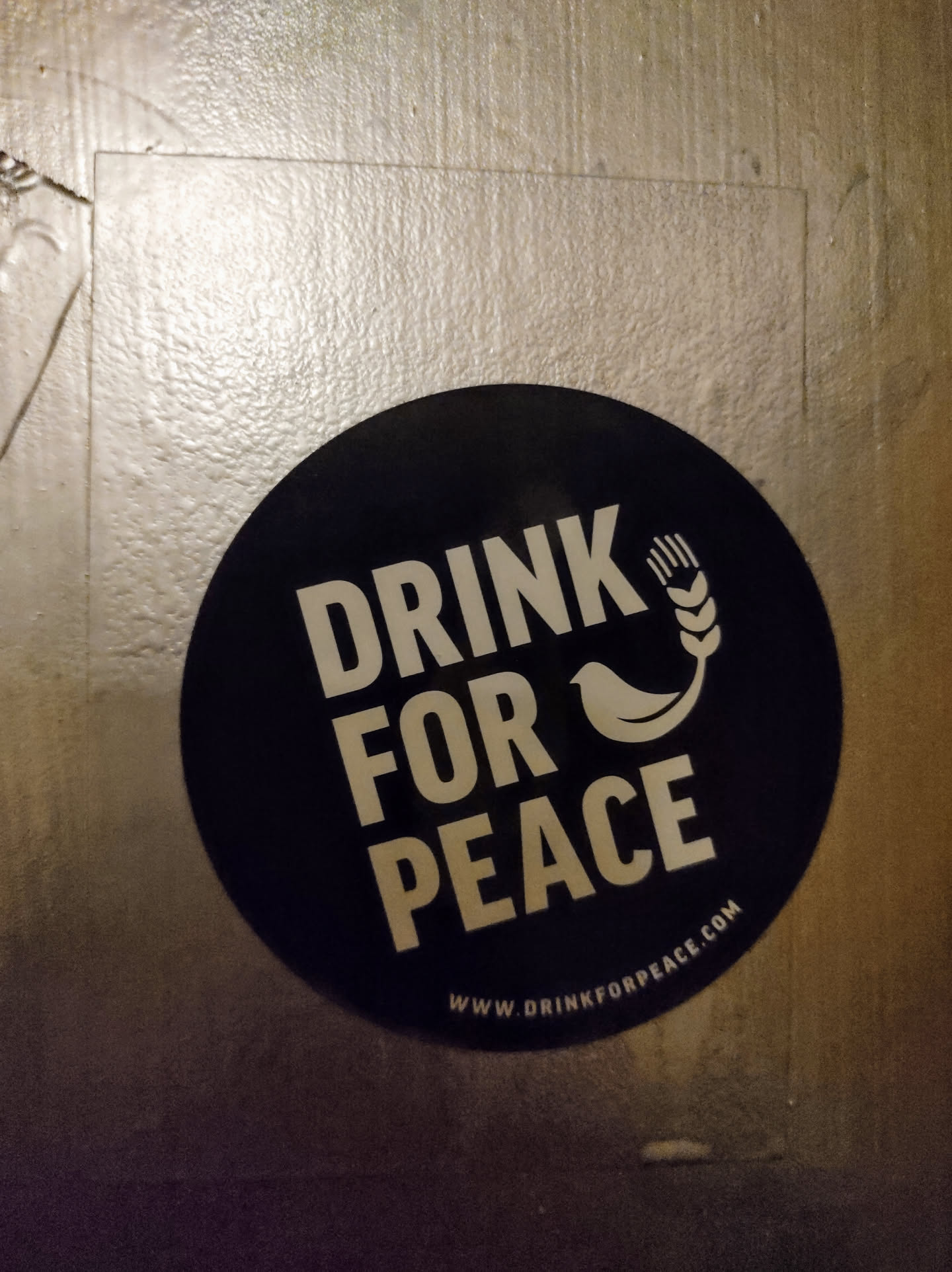 A round black sticker with the text "Drink for Peace" in white, accompanied by a small bird and wheat graphic.  The website www.drinkforpeace.com is printed at the bottom.