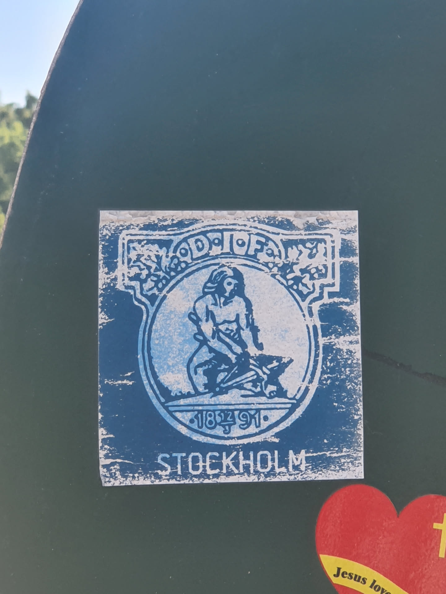 A blue and white sticker depicting a man working at an anvil, with the text "STOCKHOLM" and the years "1891-1991" underneath. The sticker appears to be vintage or retro-styled.