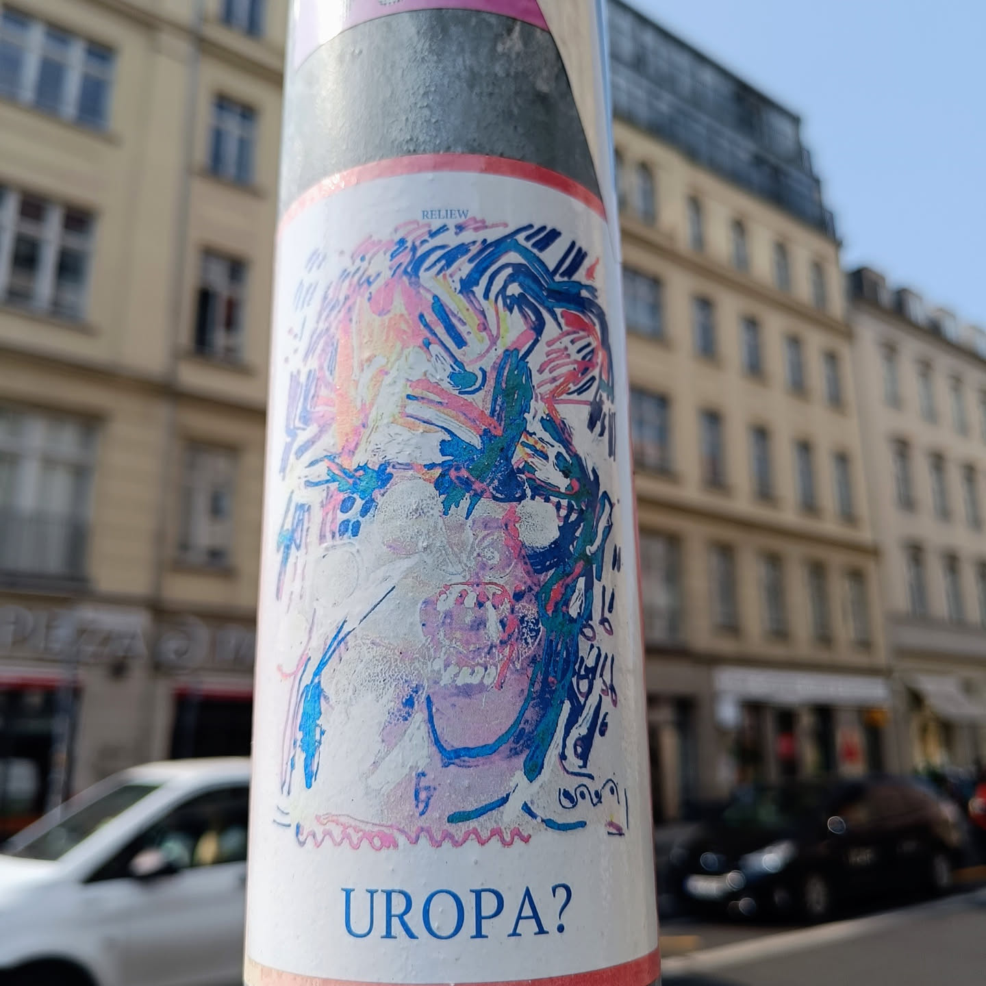 This sticker showcases an abstract artistic interpretation of a face, rendered in a blend of pastel and bold colors. The style is reminiscent of expressionism or surrealism. The word "UROPA?" is printed at the bottom, adding an element of intrigue. The sticker appears to be affixed to a pole in an urban environment.