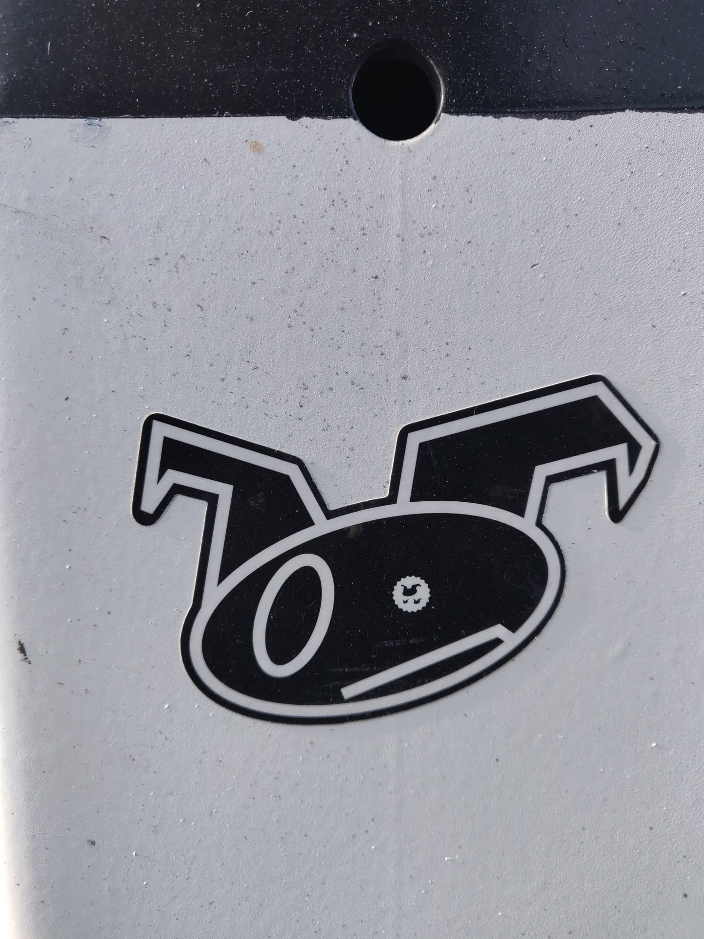 A black and white sticker featuring a stylized cartoon character with large ears and a simple face. The character's design is minimalist and geometric. The sticker is affixed to a light gray surface.