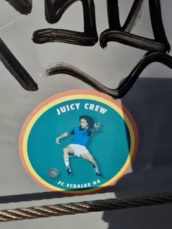 Round sticker featuring Bob Marley playing football for FC Schalke 04.  The sticker has a teal background with yellow and orange rings. The text 'Juicy Crew' is at the top and 'FC Schalke 04' is at the bottom.