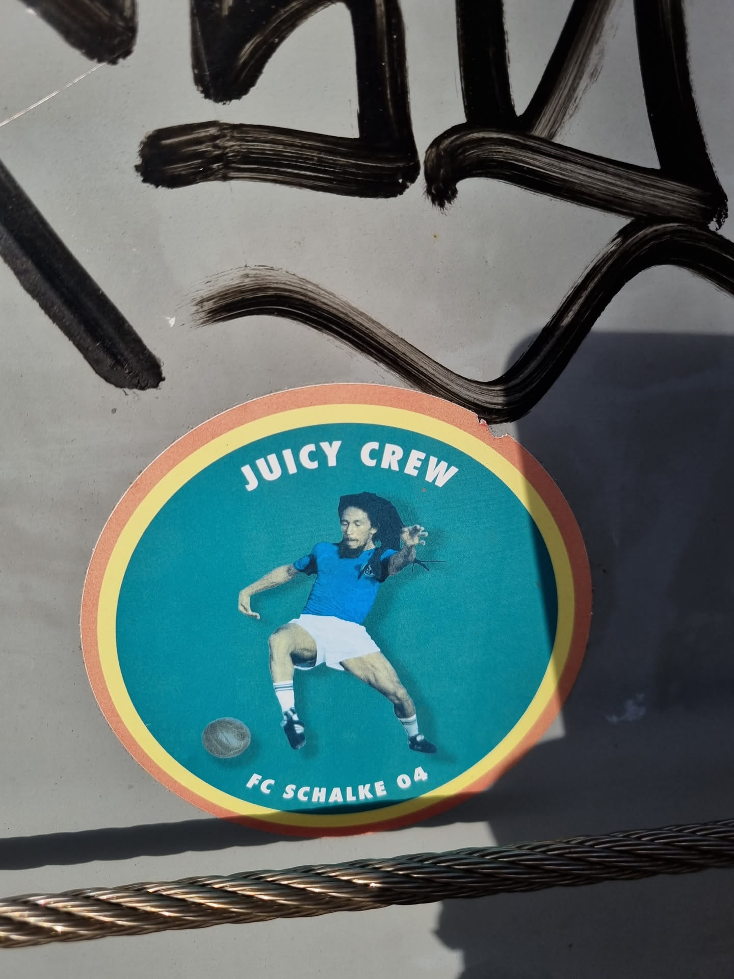 Round sticker featuring Bob Marley playing football for FC Schalke 04.  The sticker has a teal background with yellow and orange rings. The text 'Juicy Crew' is at the top and 'FC Schalke 04' is at the bottom.