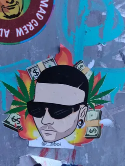 This is a sticker featuring a cartoon-like illustration of J Balvin, the famous Reggaeton singer, surrounded by money and marijuana leaves, all set in flames. The sticker has the artist's Instagram handle @p_pboi. 
