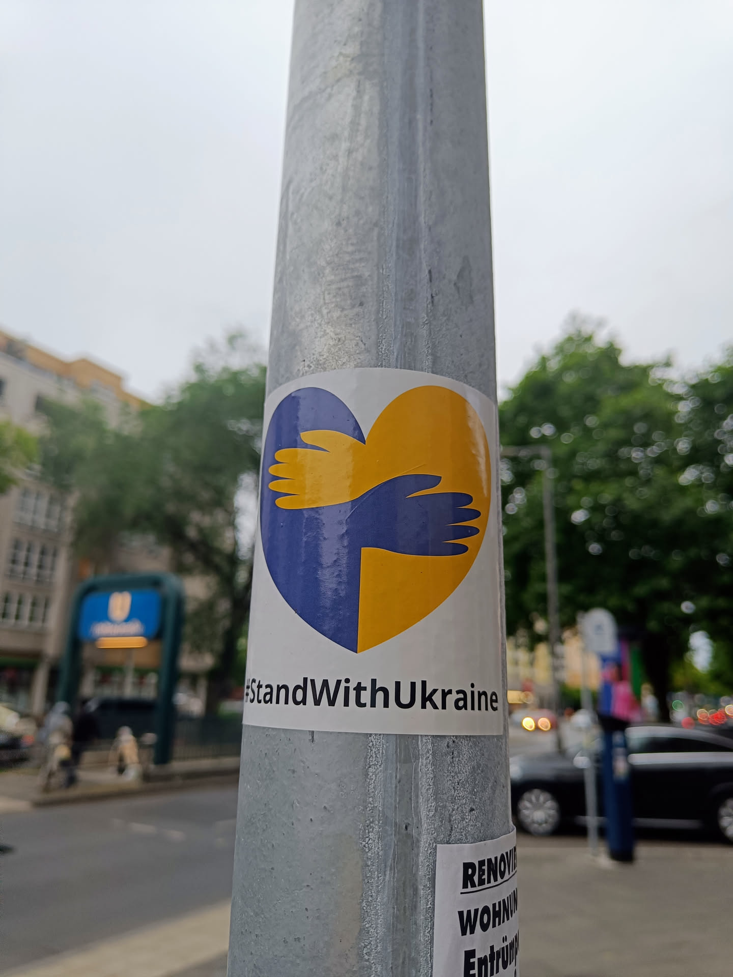 A sticker expressing solidarity with Ukraine. It features a heart-shaped design with two hands embracing, representing support and unity. The colors of the Ukrainian flag are incorporated into the design.