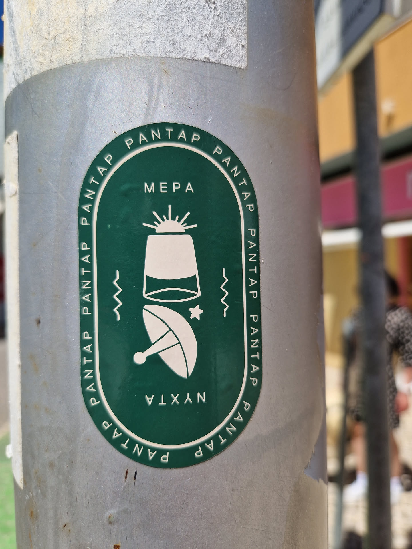 Round green sticker with illustrations of a satellite dish and what looks like a lighthouse or a small tower. The text 'PANTAP' is repeated around the edge, with 'MEPA' at the top and 'NYXTA' at the bottom. 