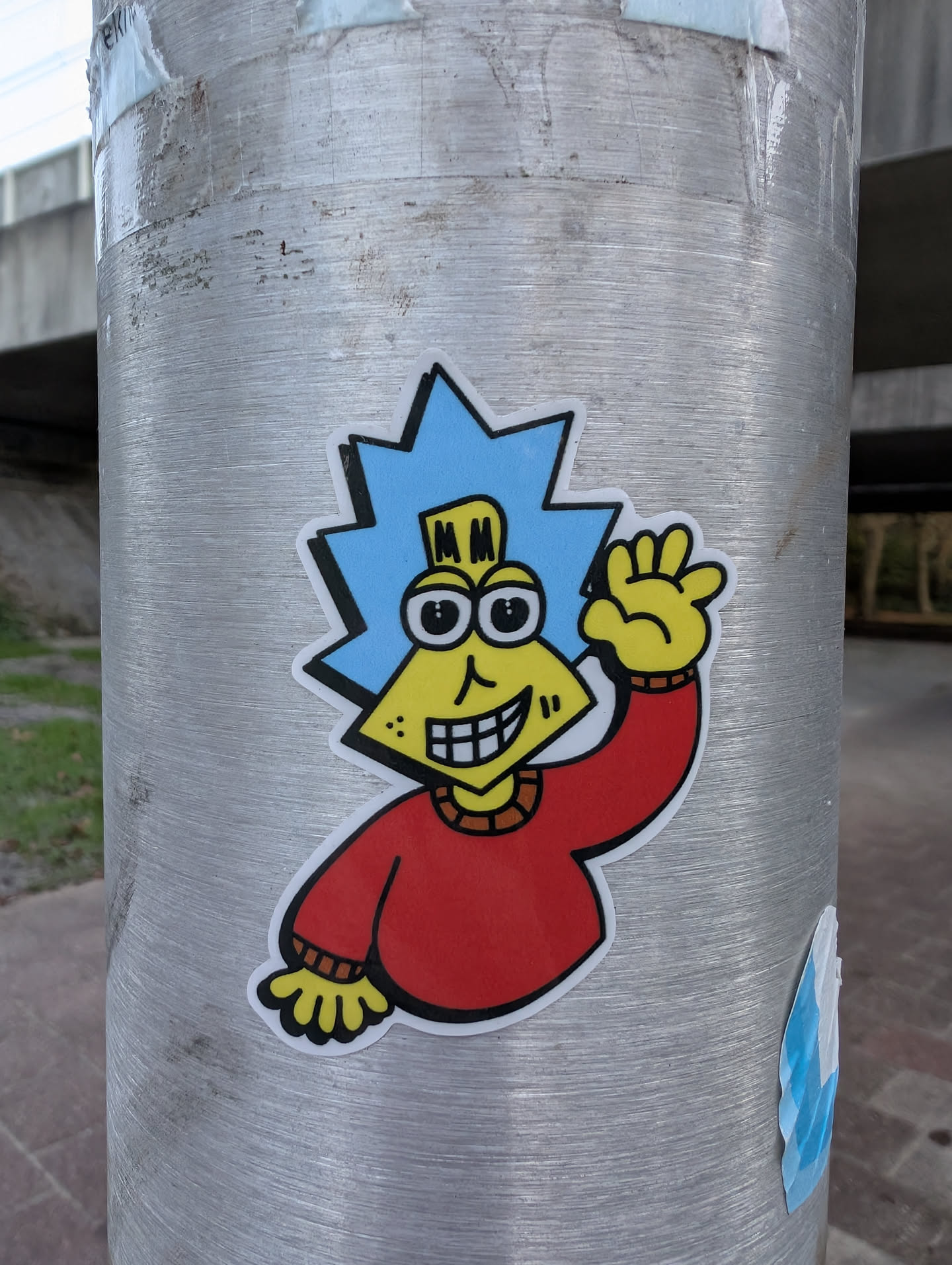 The sticker features a cartoon character with a yellow, triangular face, large black and white eyes, and a wide, toothy grin. The character has bright blue, spiky hair and is wearing a red sweater with yellow cuffs and collar details. Its right hand is raised in a wave. The sticker has a white border with a black outline.