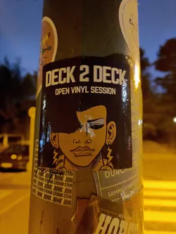 A sticker featuring a stylized illustration of a woman's face with lightning bolt earrings, promoting an open vinyl session called "Deck 2 Deck".