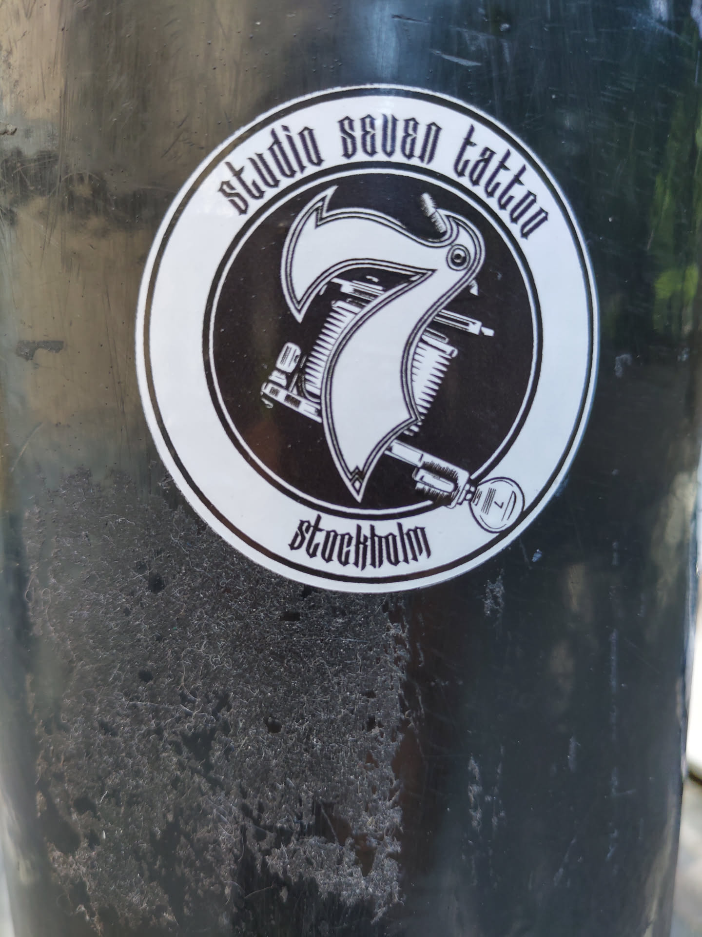 Black and white sticker with the logo of Studio Seven Tattoo in Stockholm. The logo features a stylized number seven incorporated into a tattoo machine design. 
