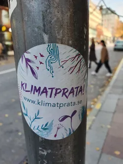 Round sticker with a nature and technology design.  Features text in Swedish, "Klimatprata!" and a website address.