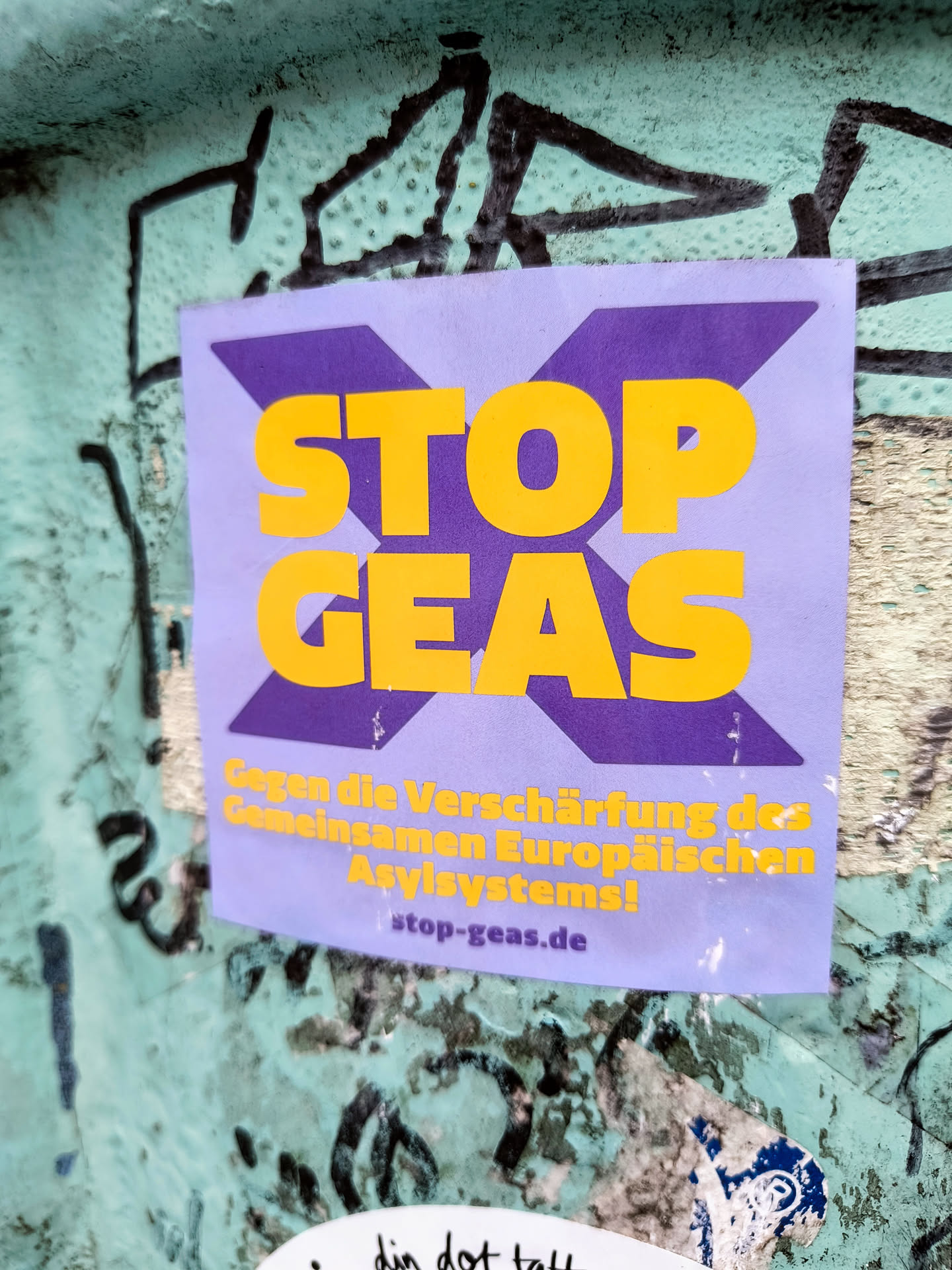 A sticker with the text 'STOP GEAS' in bold yellow letters on a purple background.  The smaller text below reads 'Gegen die Verschärfung des Gemeinsamen Europäischen Asylsystems!' which translates from German to "Against the tightening of the Common European Asylum System!"  A website address, stop-geas.de, is also included.
