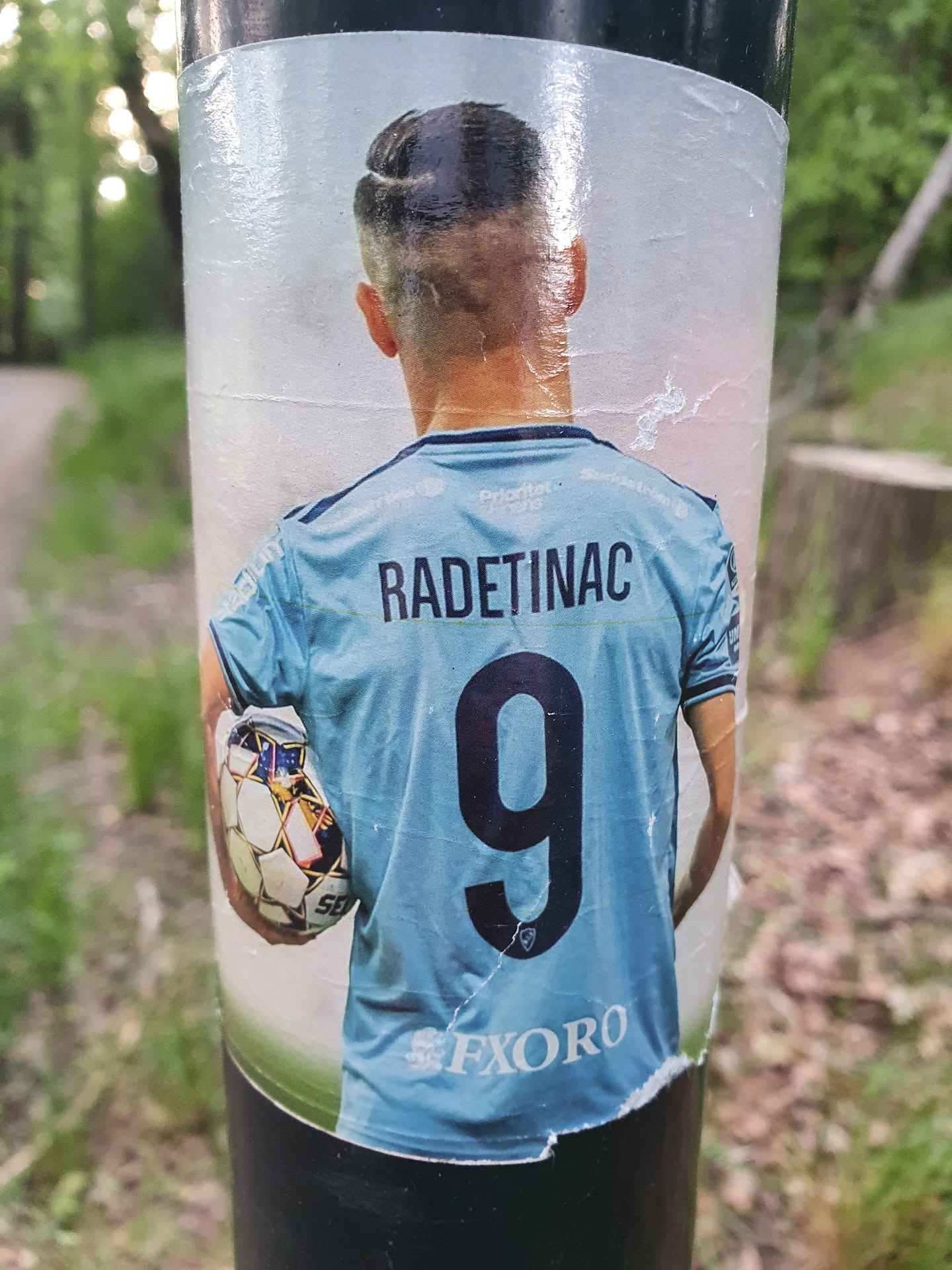 A sticker featuring the back of a soccer player's jersey with the name RADETINAC and the number 9. The player is holding a soccer ball.  The sticker shows some wear and tear from being affixed to a pole.