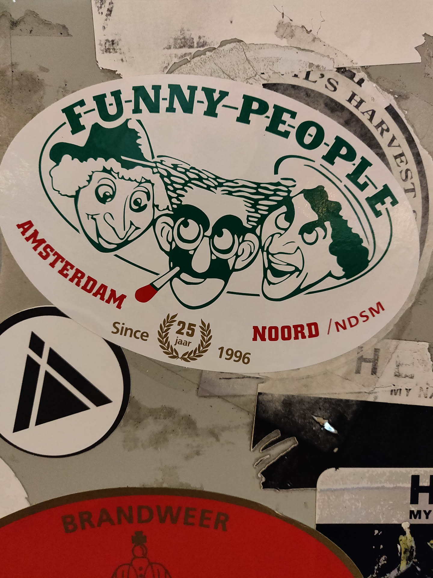 Oval sticker featuring three cartoon faces with the text 'FUNNY-PEOPLE' at the top and 'AMSTERDAM' at the bottom. It also includes 'Since 1996' and a 25th-anniversary logo.