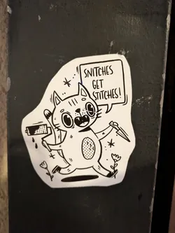 A black and white sticker featuring a cartoon cat holding a paint roller and a knife. The cat has a speech bubble above it that says "Snitch get stitches!"
