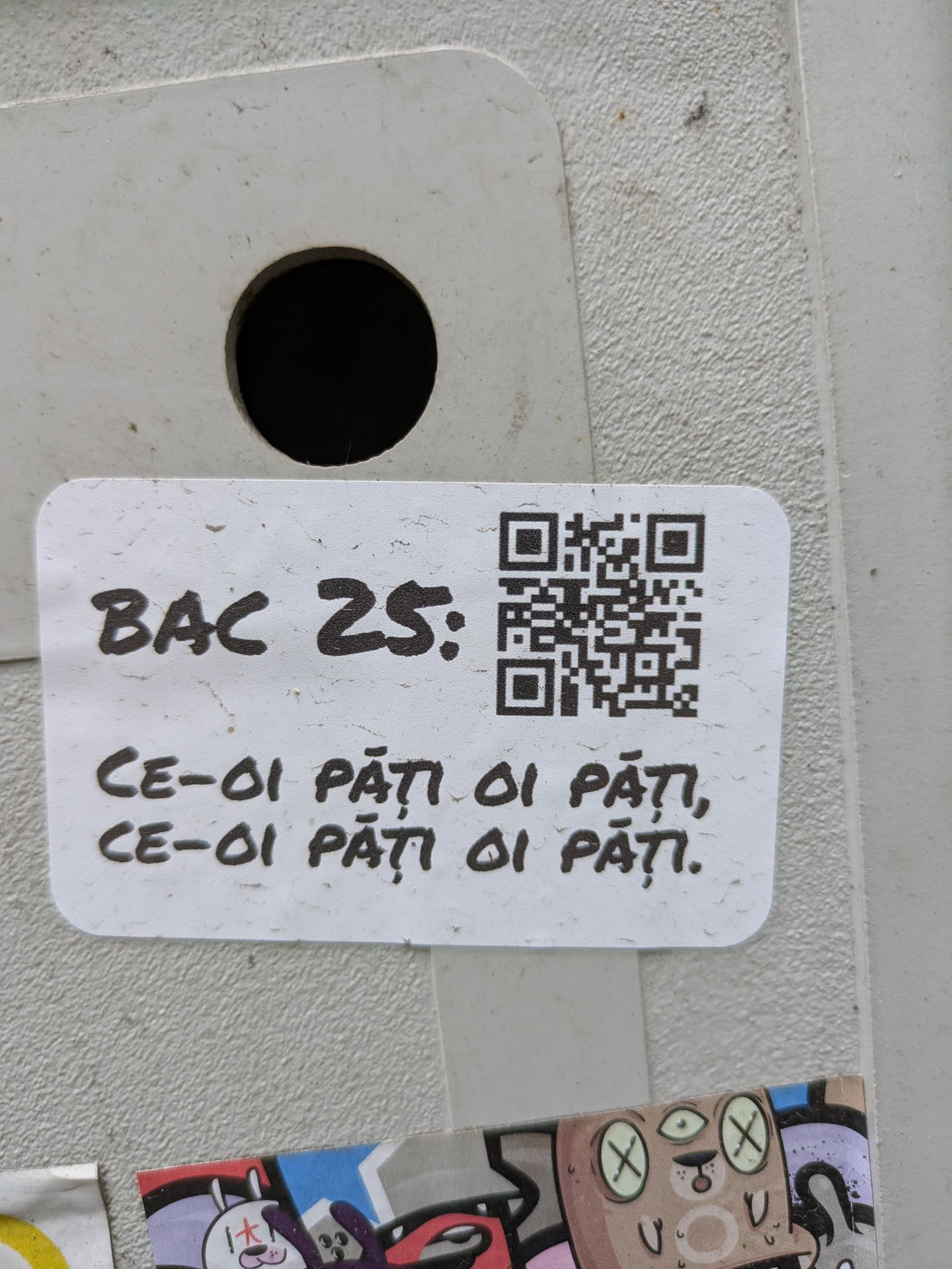 A white sticker with a QR code and text 'BAC 25:' followed by the Romanian phrase 'CE-OI PĂȚI OI PĂȚI, CE-OI PĂȚI OI PĂȚI.'