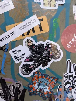 A sticker featuring a cartoon illustration of a woman riding a motorcycle.  The text on the sticker reads 'The 'rents go Racing Team'.