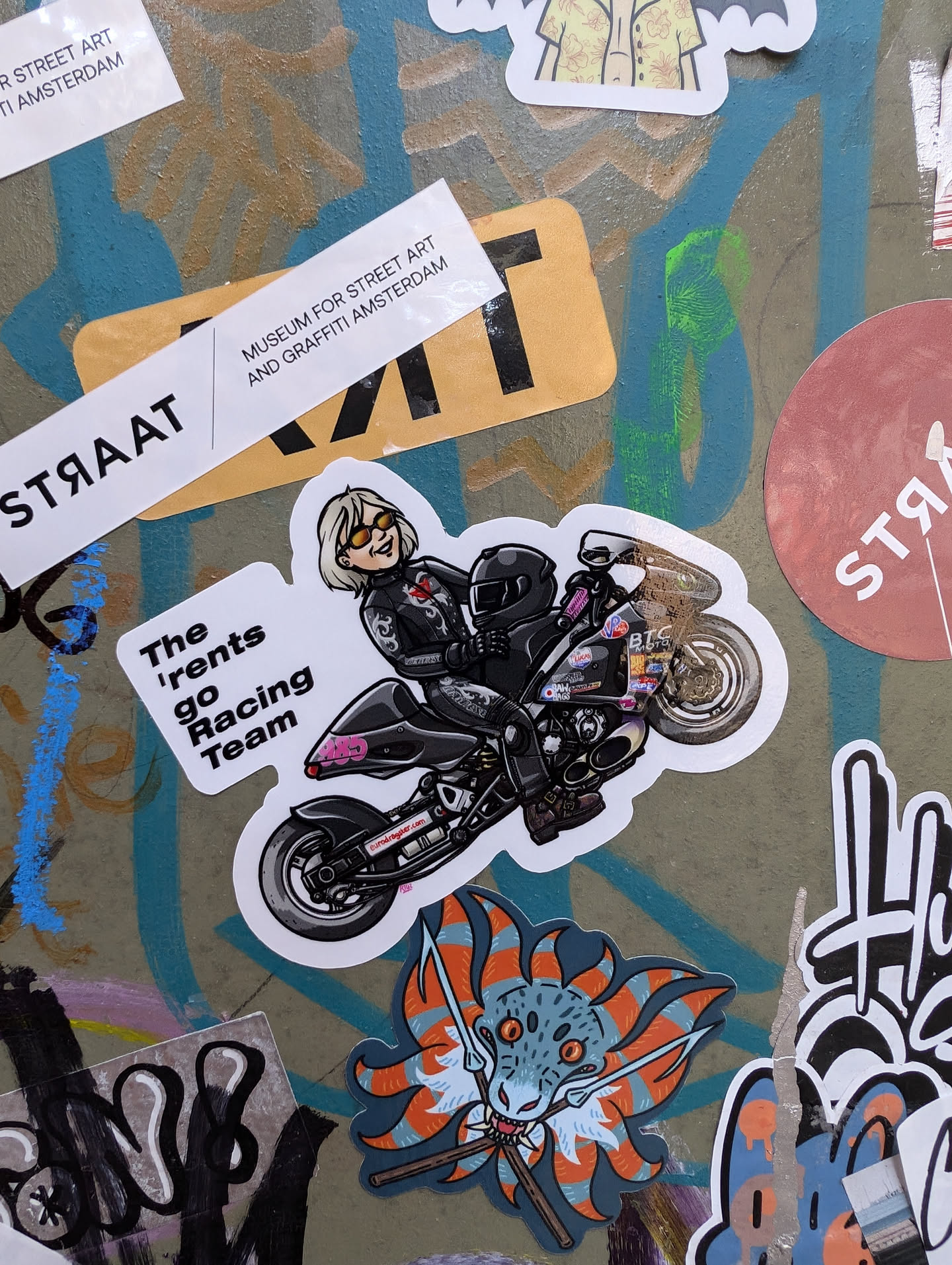 A sticker featuring a cartoon illustration of a woman riding a motorcycle.  The text on the sticker reads 'The 'rents go Racing Team'.
