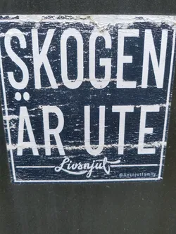 A dark blue sticker with white text. The text says "SKOGEN ÄR UTE" (The forest is out) and has the signature "Livsnjut" with the Instagram handle @livsnjutfamily. The sticker shows some signs of wear.