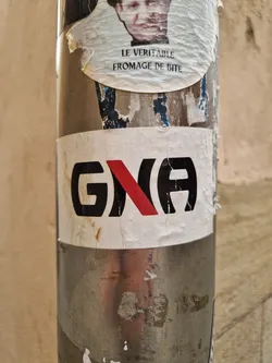 A sticker with the logo G(X)A on a metallic pole. The logo is black and red. The sticker is slightly damaged.