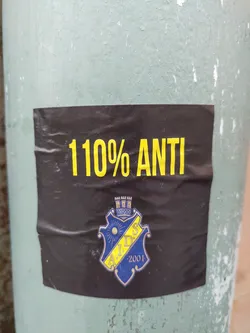 Black sticker with yellow text that says "110% ANTI" and a blue and yellow crest with the letters A.I.D.S and the number 2001. 