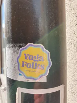 A yellow and purple sticker with the text 'Yoga Folks' and the website address 'www.yogafolks.se'. The sticker has a slightly wavy, flower-like border.