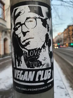 Black and white sticker with an illustration of a person wearing glasses and a hat. The text 'Vegan Club' is prominently displayed at the bottom, along with a website address: www.onelifeonechance.com. Smaller text is visible on the illustration, including the word 'LOVE'.