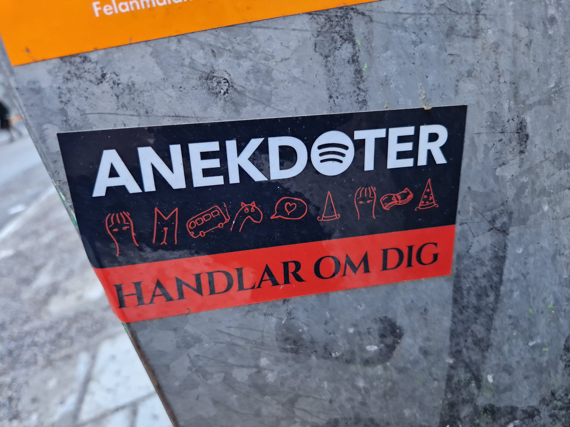 Black and red sticker with the text "ANEKDOTER" and  "HANDLAR OM DIG" in white. There are small icons in between the texts.  The Spotify logo is visible next to the word Anekdoter. 