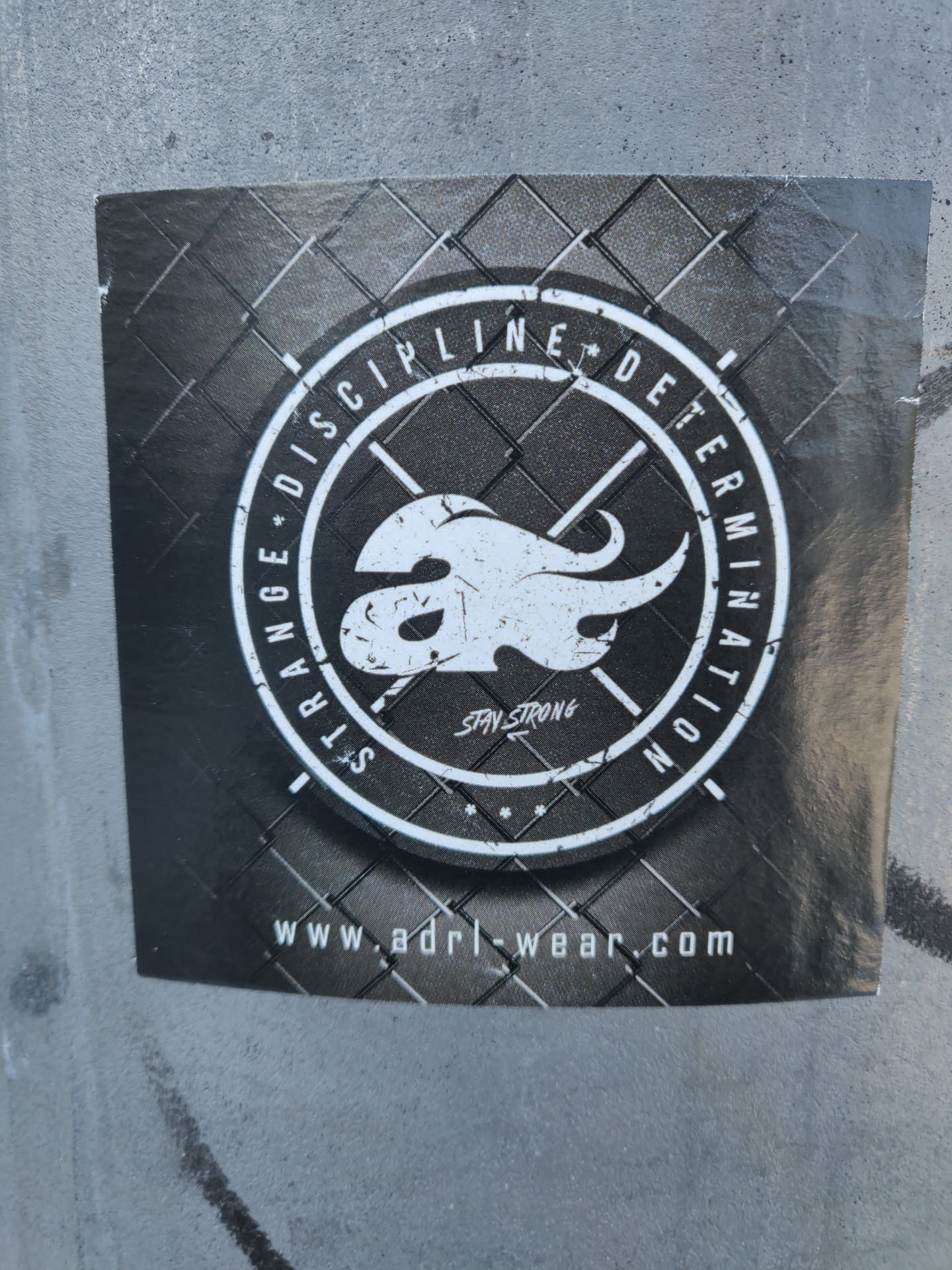 A black and white sticker with a logo featuring a stylized flame and the words 'Discipline' and 'Determination' surrounding it. The text 'Stay Strong' is in the center.  A website address is printed at the bottom.