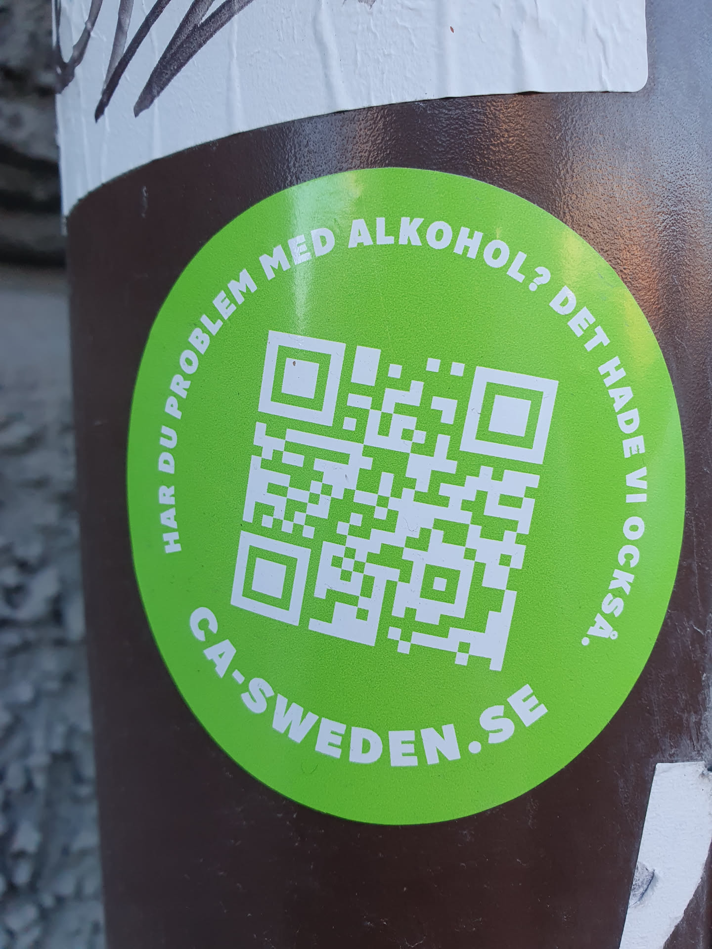 A green circular sticker with a QR code in the center. The text around the QR code says in Swedish: "Har du problem med alkohol? Det hade vi också." which translates to: "Do you have a problem with alcohol? We did too."  The bottom of the circle says ca-sweden.se