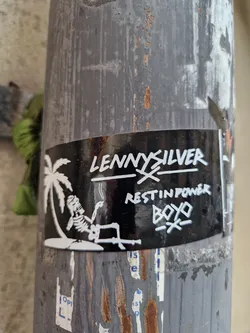 Black and white sticker with an illustration of a skeleton relaxing under a palm tree on a beach. The text 'LENNY SILVER' is written at the top, followed by 'REST IN POWER BOYO'.