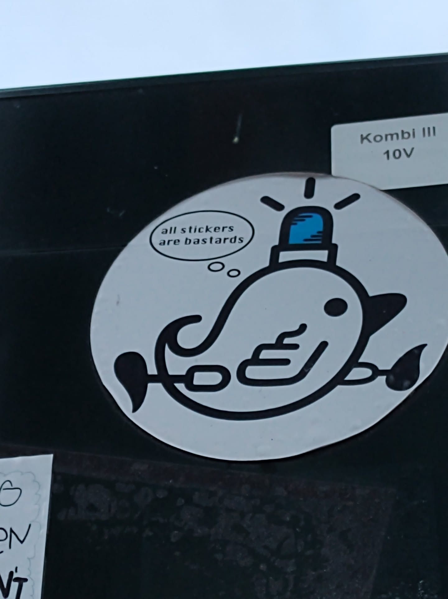 Round sticker depicting a stylized whale with a police light on its head. The whale is drawn in black and white, with a speech bubble above it that reads: "all stickers are bastards".
