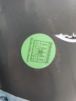 A light green circular sticker with a black and white line drawing of a building and the text "Hallwylska museet" written vertically along the left side.