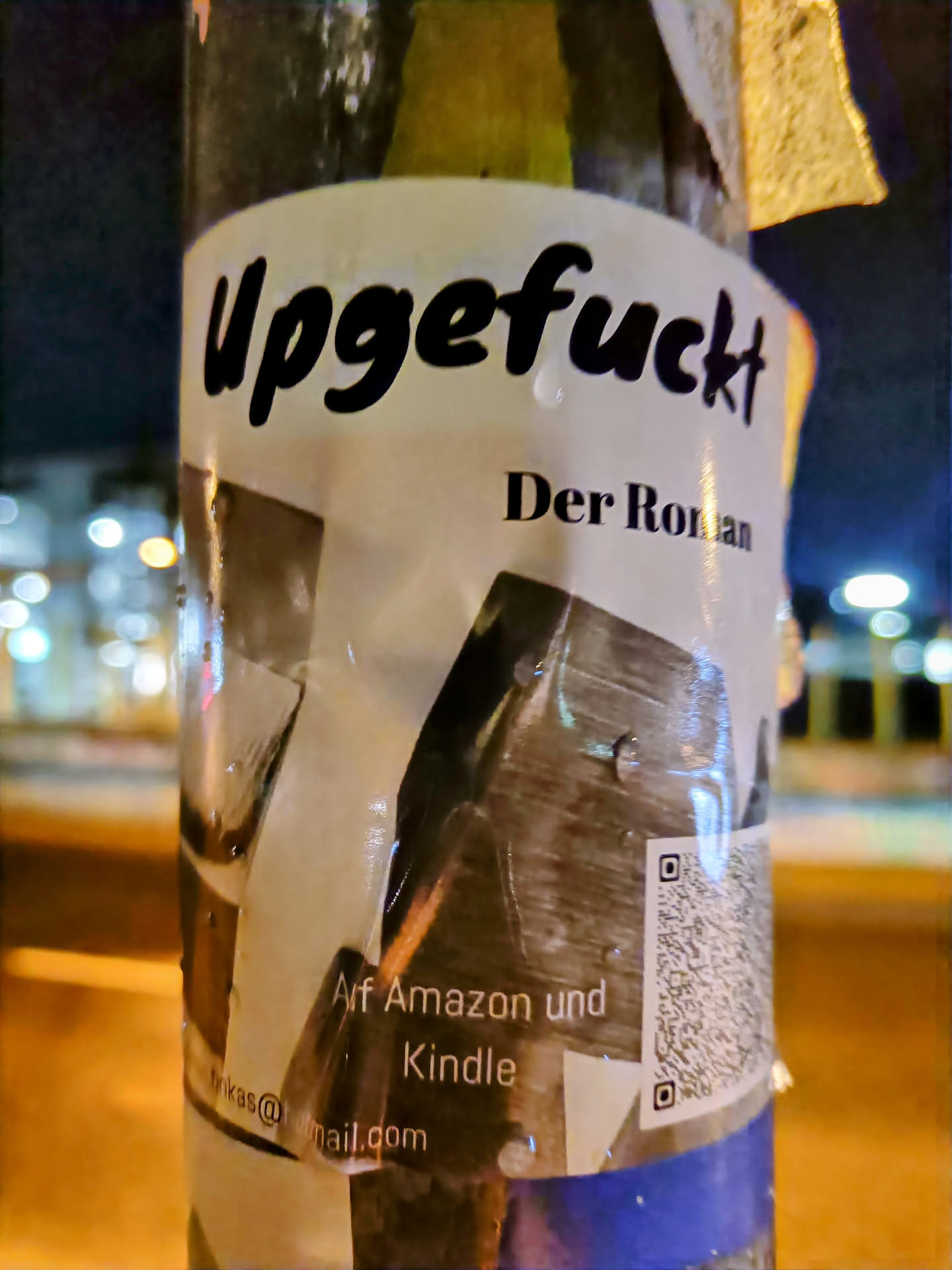 A sticker advertising a book titled "Upgefuckt Der Roman" which is available on Amazon and Kindle.  The sticker includes a QR code.