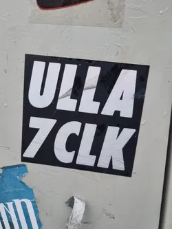 A black and white sticker with the text "ULLA 7CLK" in a bold, sans-serif font. The sticker is affixed to a light gray surface.