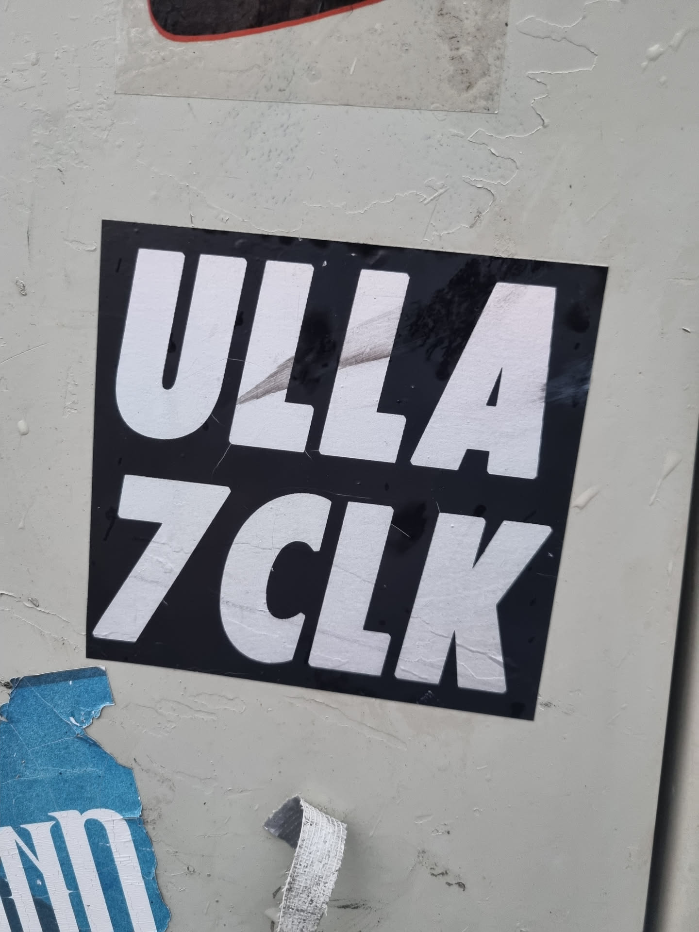 A black and white sticker with the text "ULLA 7CLK" in a bold, sans-serif font. The sticker is affixed to a light gray surface.